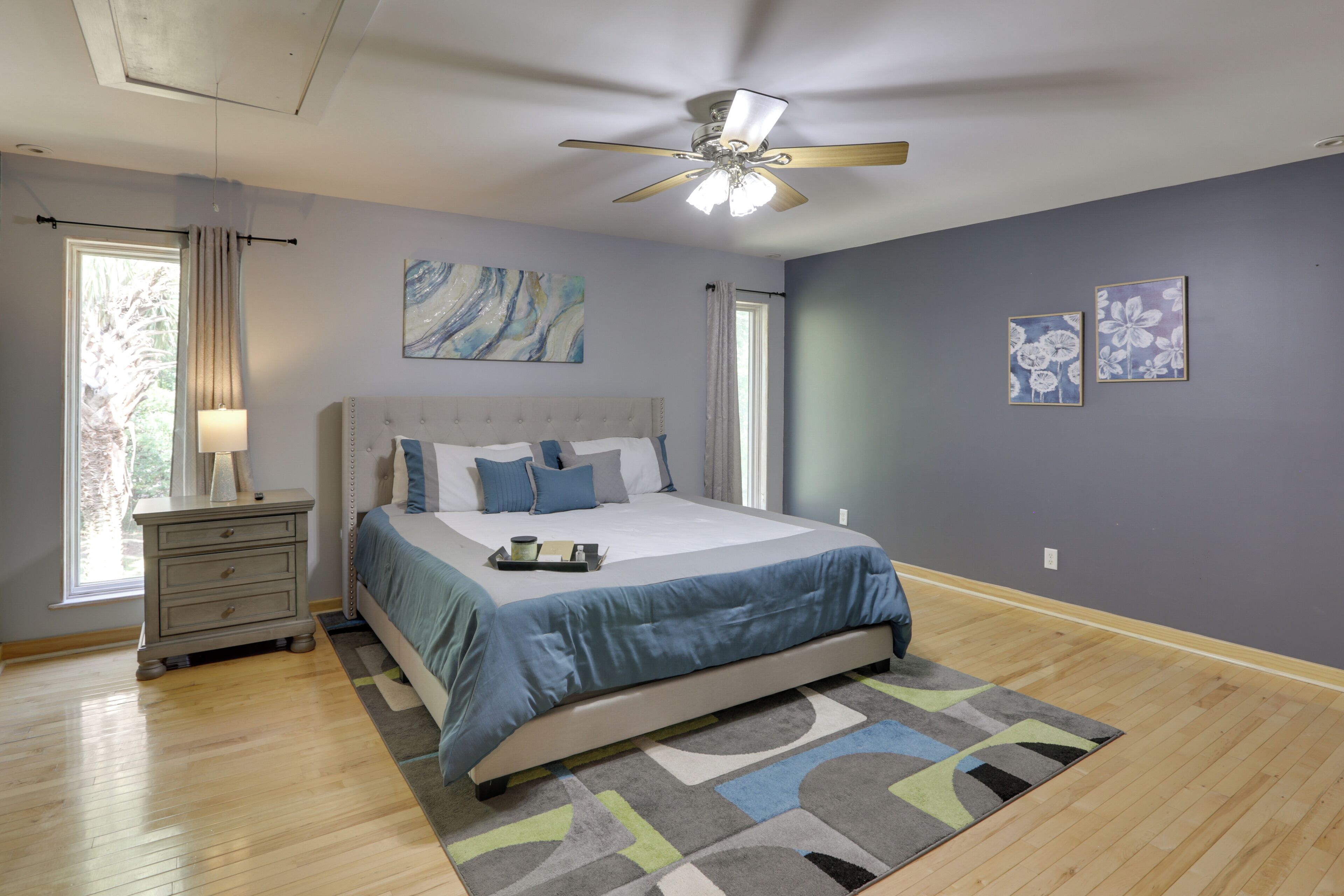 Une chambre à coucher avec un lit, une table de chevet, un ventilateur de plafond et des œuvres d’art accrochées aux murs.