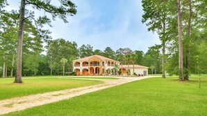 A large, two-story house with a red roof and beige walls, surrounded by a well-maintained lawn and tall trees. - Spacious Georgia Vacation Rental w/ Large Deck (Leesburg)