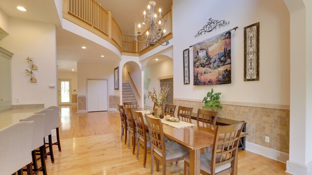A spacious dining area with a wooden table and chairs, a chandelier, and a staircase leading to an upper level. - Spacious Georgia Vacation Rental w/ Large Deck (Leesburg)