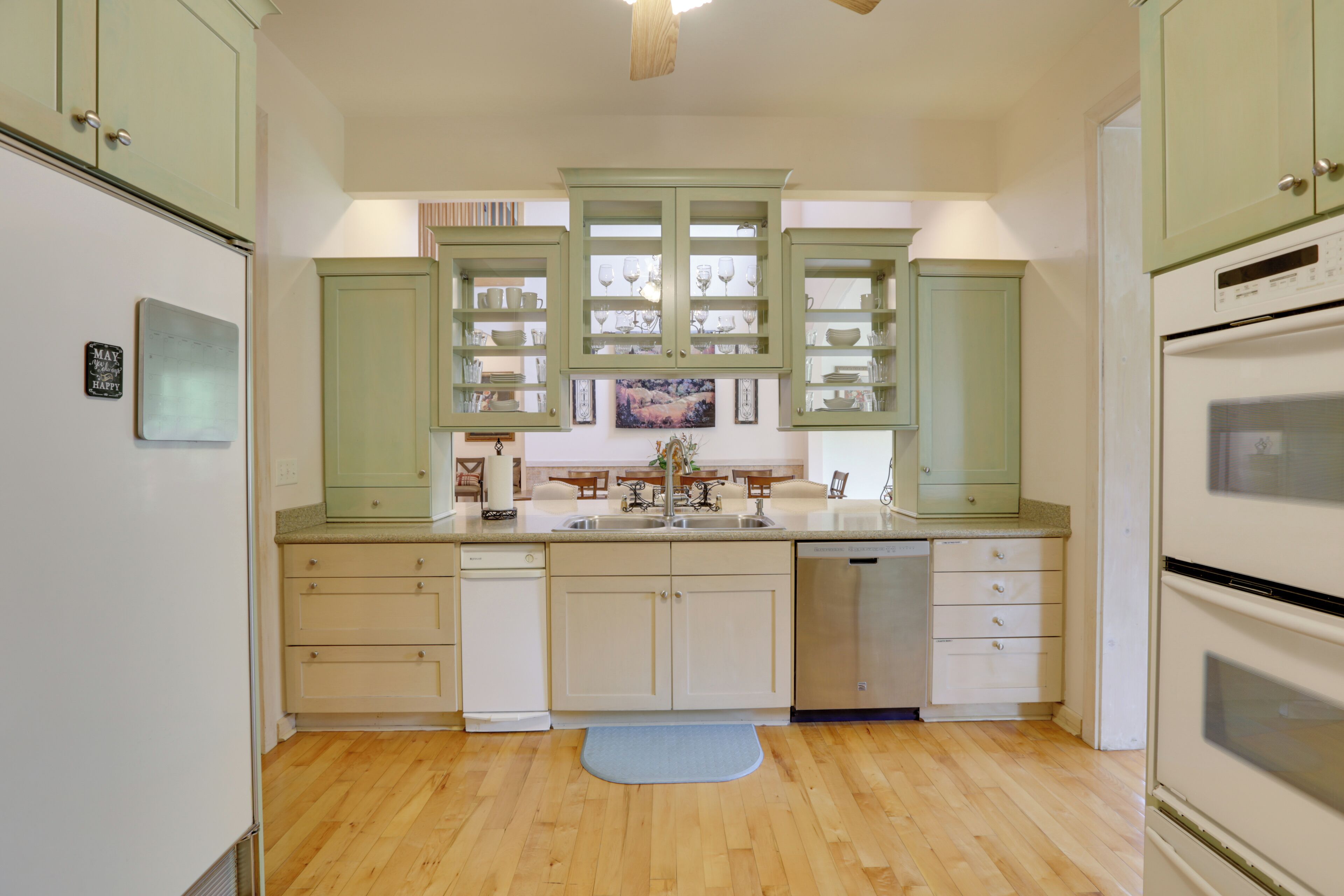 Una cocina con gabinetes verde claro, un refrigerador blanco, un lavavajillas y un horno doble.