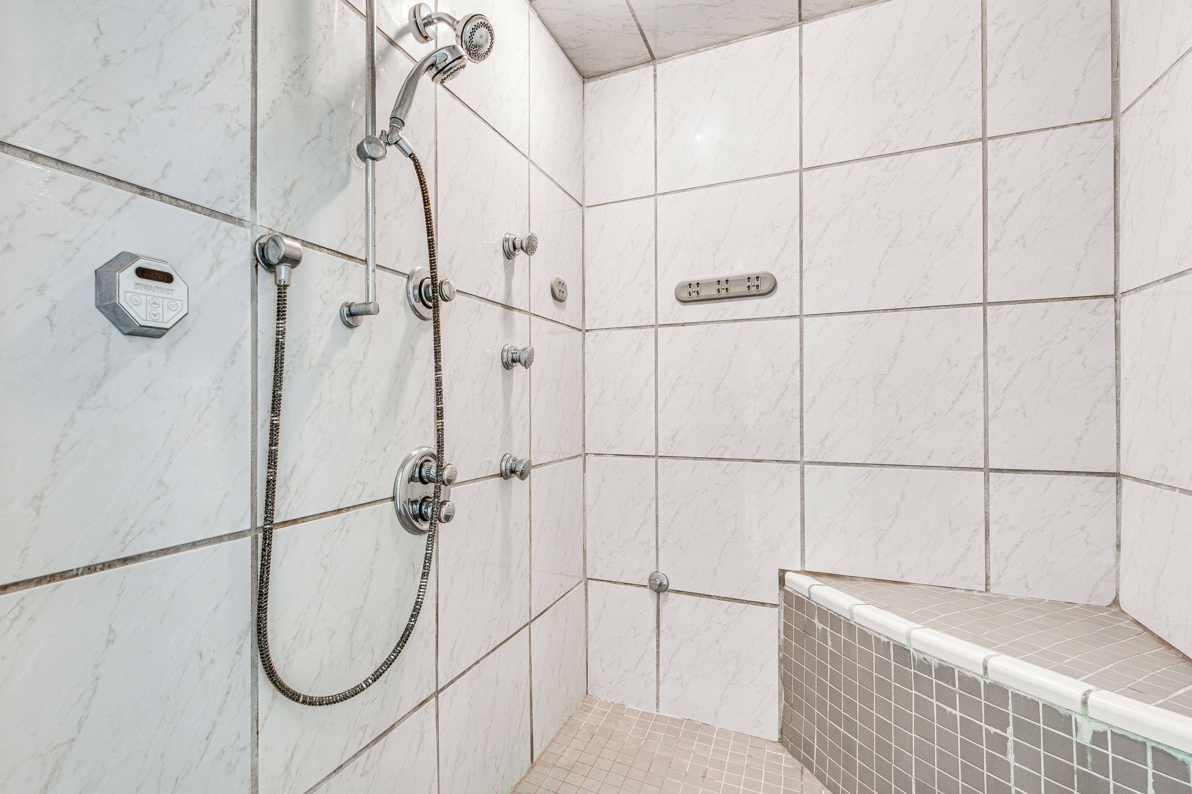 Um banheiro moderno com chuveiro, painel de controle e piso revestido de azulejos.
