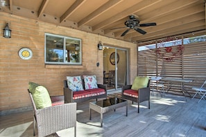 An outdoor patio with wicker furniture, a ceiling fan, and a brick wall.