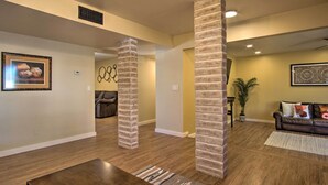 A spacious living room with wooden flooring, brick pillars, a leather sofa, and a coffee table. - Eastside Home w/ Pool Near Hiking! (Tucson)