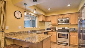 A kitchen with granite countertops, stainless steel appliances, wooden cabinets, and a clock on the wall. - Eastside Home w/ Pool Near Hiking! (Tucson)