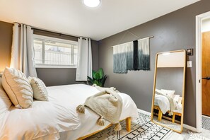 Quarto com cama, espelho, janela com cortinas e uma planta.