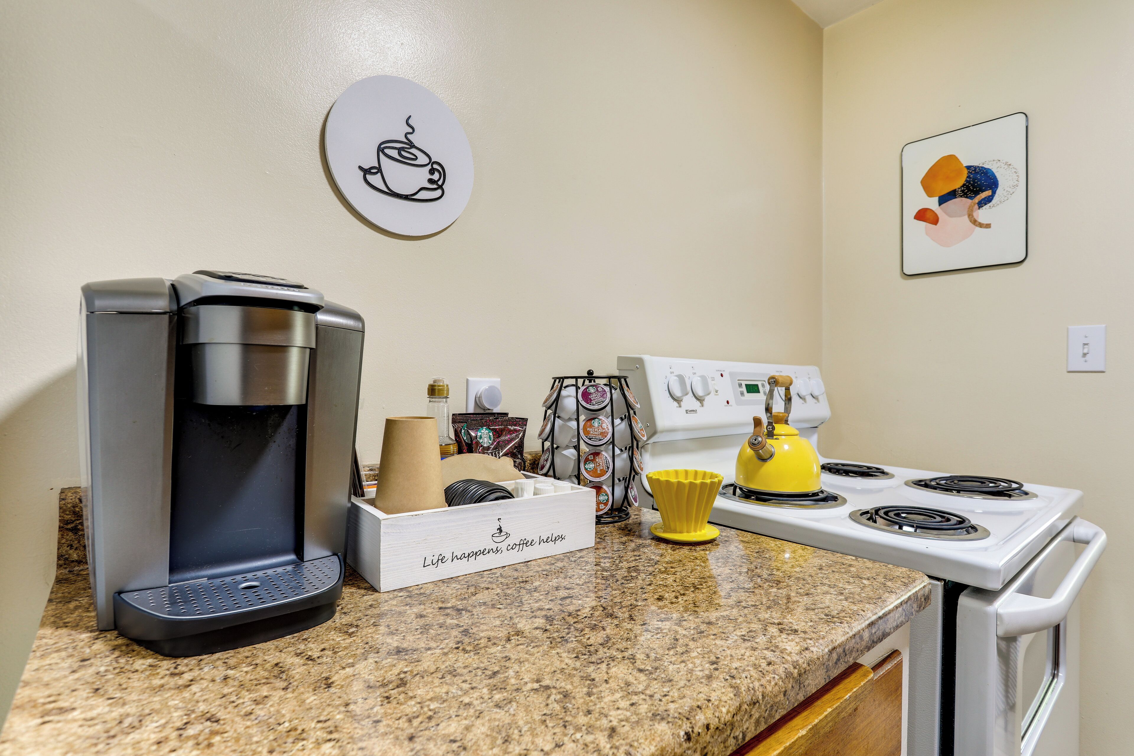 A kitchen with a coffee maker, a kettle, and a stove.