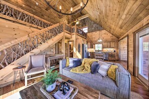 A cozy cabin interior with a wooden staircase, a living area with a sofa and armchair, and a kitchen in the background. - Stunning Escape w/ Loft, Hot Tub + Mtn Views! (Morganton)