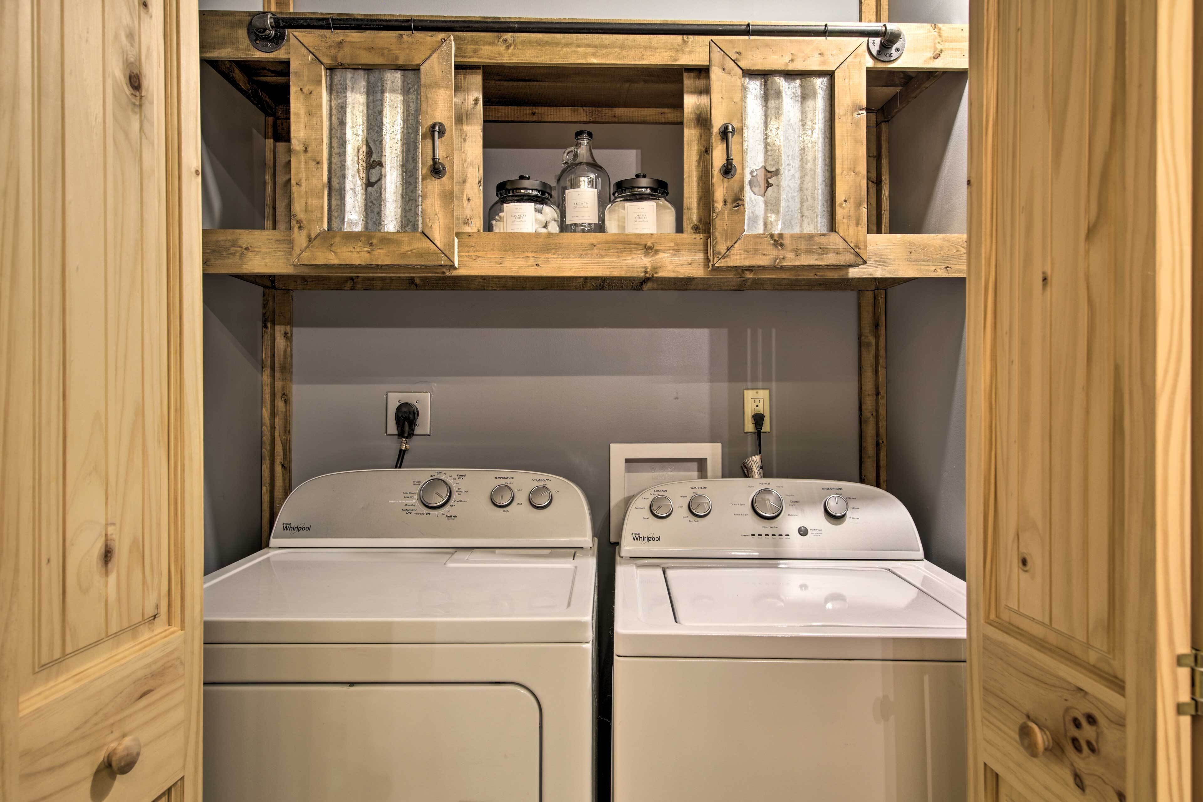Ein Waschraum mit zwei weißen Whirlpool Waschmaschinen und Trocknern, Holzschränken darüber und einem Metallregal mit Gläsern.