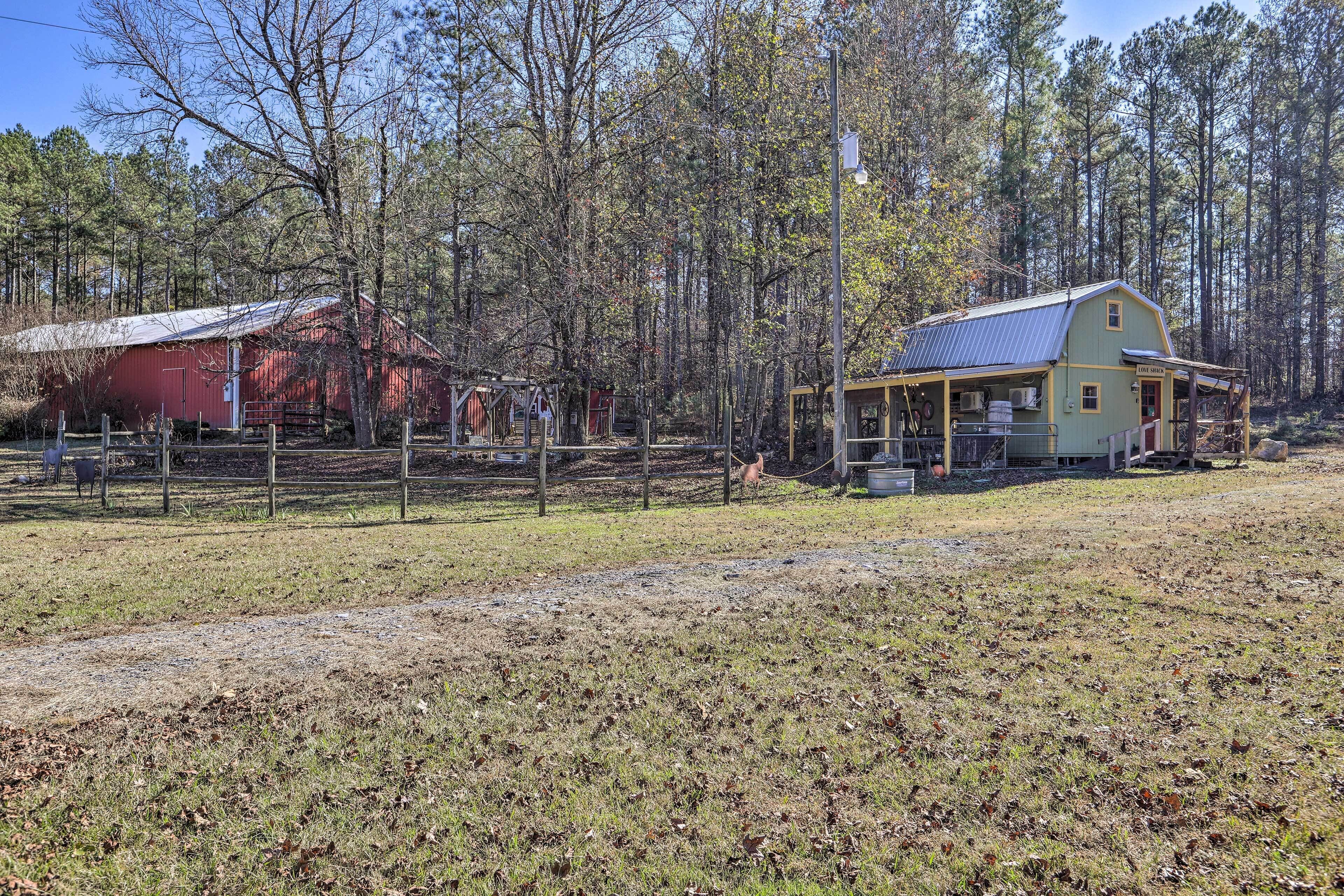 A rustic barn and a house with a porch, surrounded by a fenced pasture and trees.