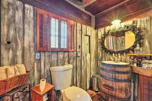 Une salle de bain rustique avec des murs en bois, des toilettes blanches, un lavabo en forme de tonneau en bois et un miroir doté d'un cadre décoratif.