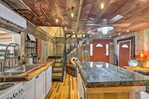 A rustic kitchen with a wooden countertop, a stove, and a sink. There is a staircase leading to a second floor with a red door. - Georgia Farm Vacation Rental Cabin ~ 12 Mi to Rome (Aragon)