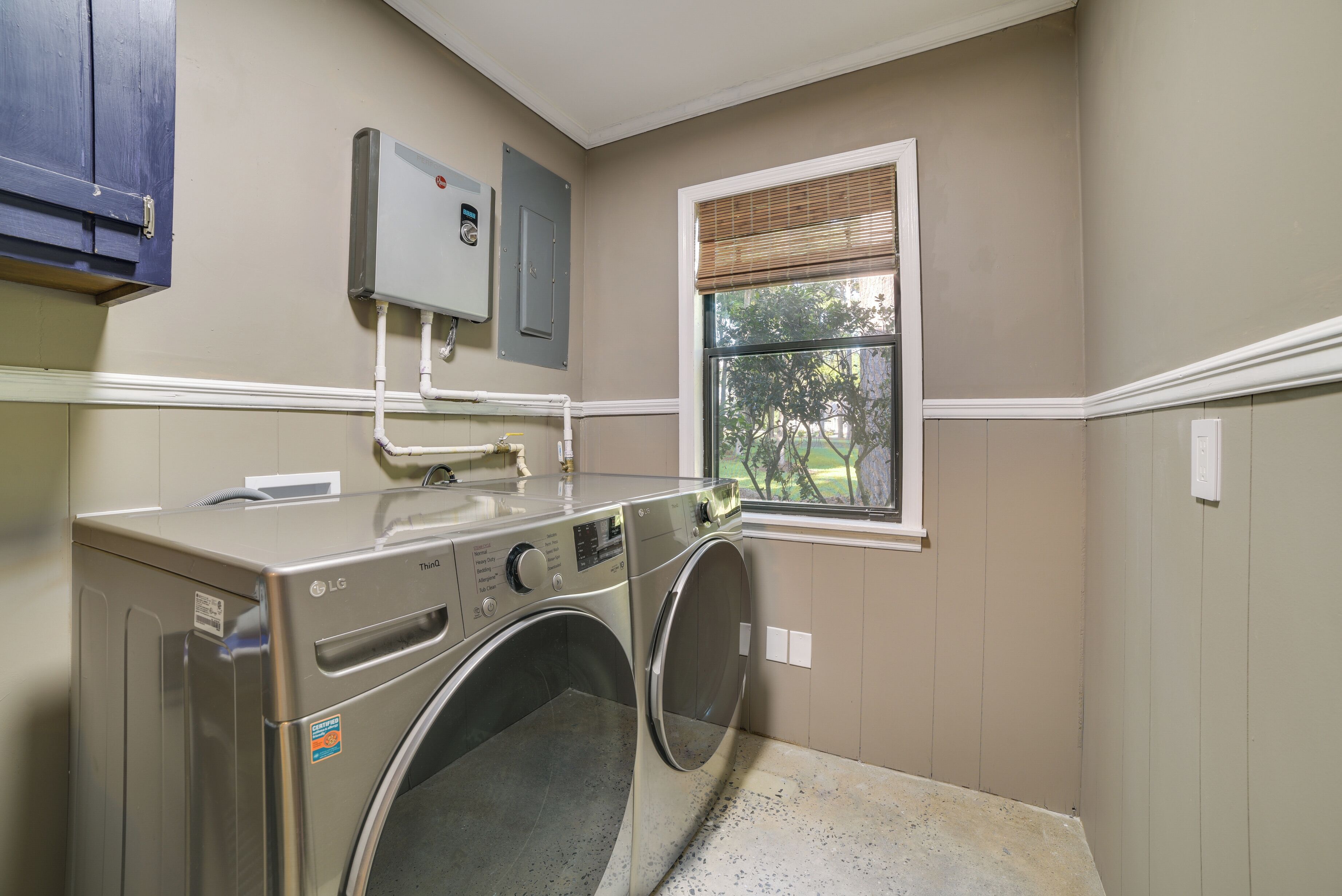 A laundry room with two stacked front-loading washers and dryers, a window with blinds, and a utility meter on the wall.