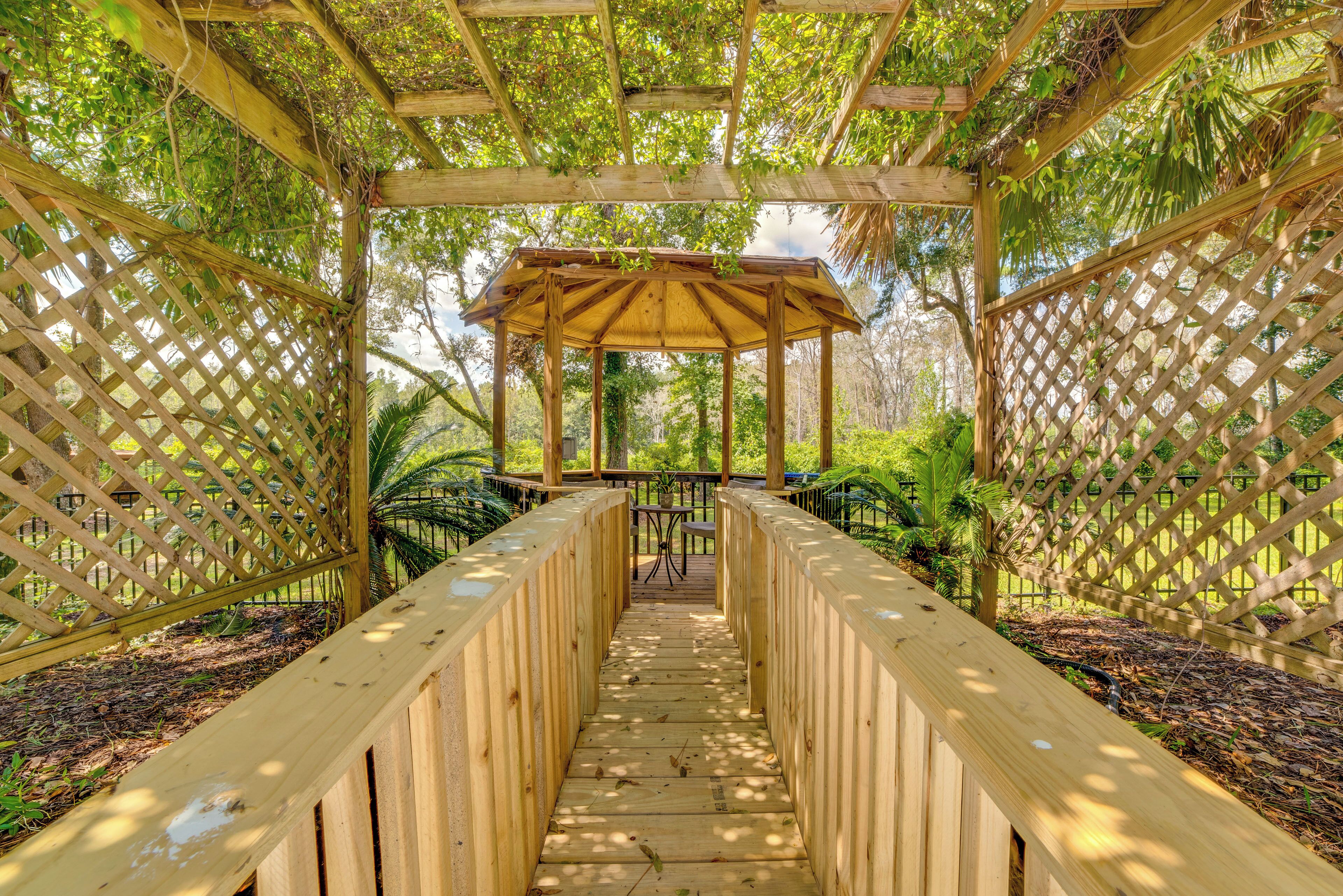 A wooden gazebo with a bench in the center, surrounded by a wooden fence and lush greenery.