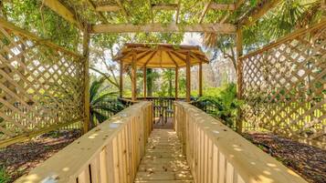 A wooden gazebo with a bench in the center, surrounded by a wooden fence and lush greenery.