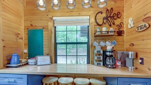 A wooden cabin interior with a kitchen counter, stools, and a coffee sign.
