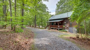 A cabin with a gravel driveway leading to a wooden porch, surrounded by dense trees.