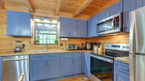 A modern kitchen with blue cabinets, stainless steel appliances, and wooden flooring.