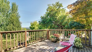 A wooden deck with a railing, two chairs, and a potted plant with flowers. - Historic Seattle Vacation Rental in Seward Park! (Seattle)