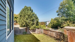 A backyard with a wooden fence, a large tree, and a house with a sloped roof. - Historic Seattle Vacation Rental in Seward Park! (Seattle)