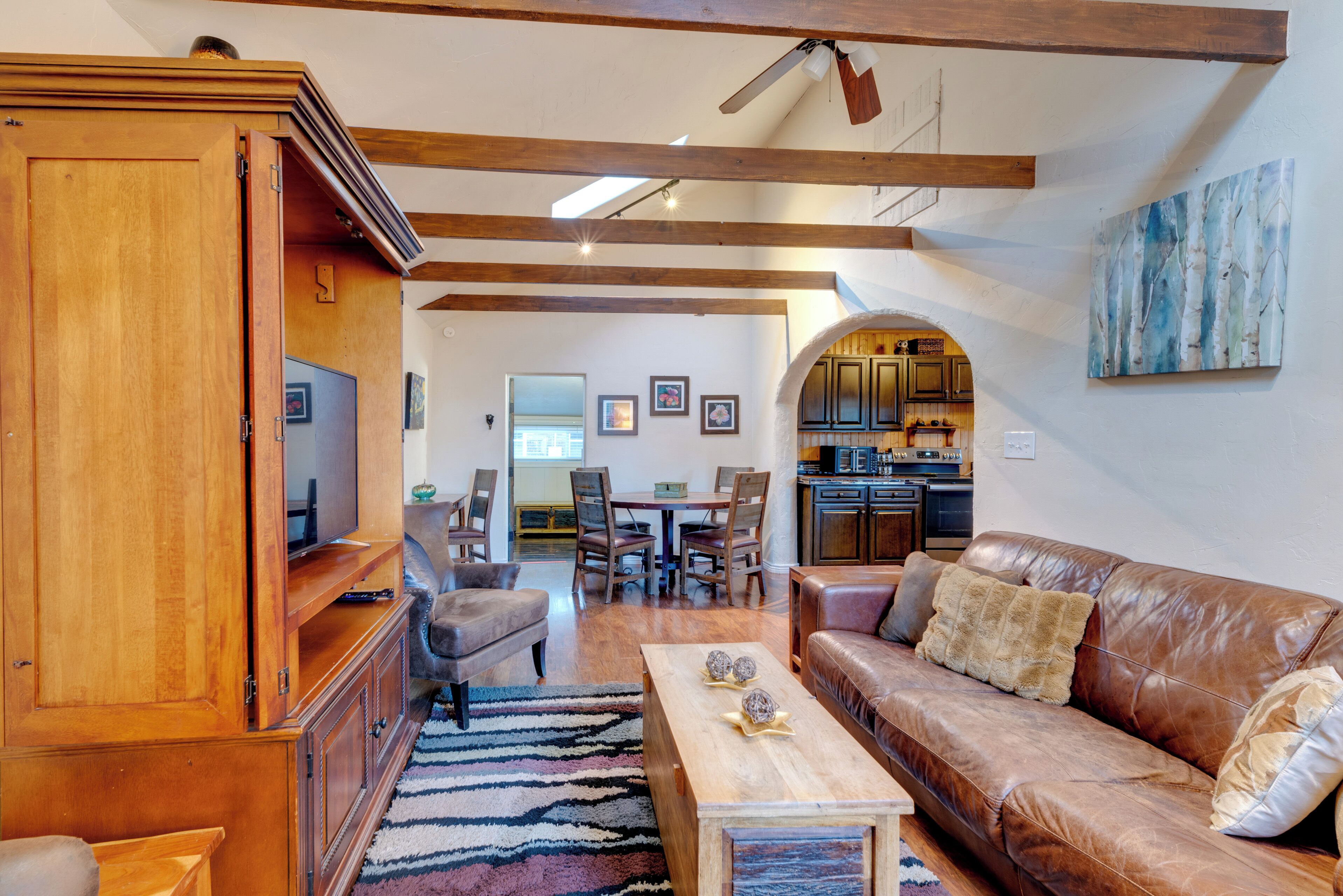 Un salón espacioso con sofá de cuero marrón, centro de entretenimiento de madera y zona de comedor con sillas y mesa.