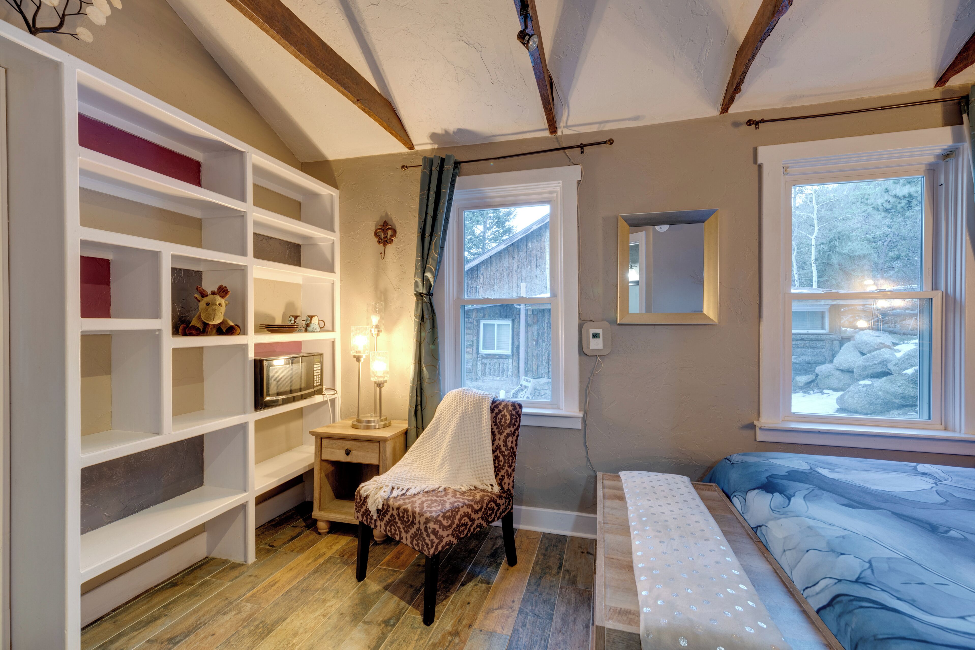 Un dormitorio acogedor con cama, una silla, estanterías y una ventana con vistas a árboles.