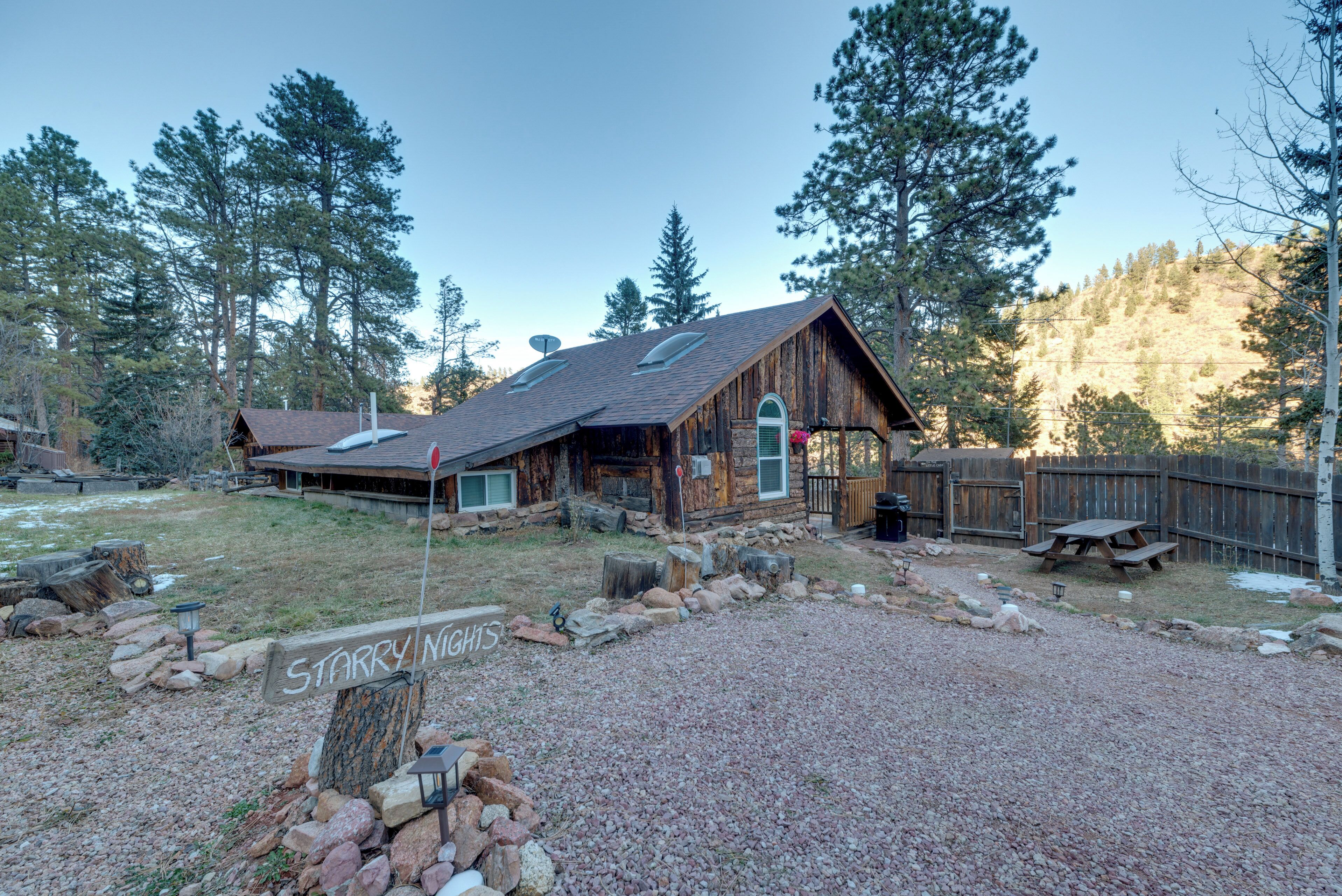 A rustic cabin with a gravel driveway, wooden deck, and a stone wall.