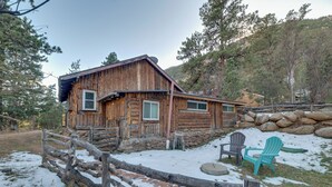 Une cabane rustique en rondins de bois, avec des fondations en pierre, une véranda en bois et un sol recouvert de neige.