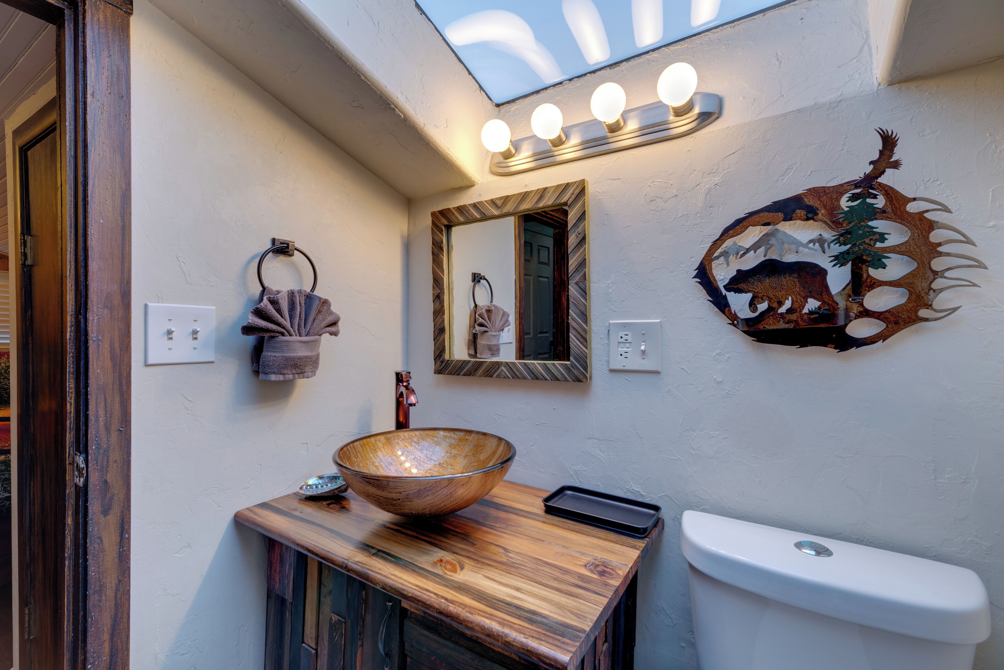 A bathroom with a wooden vanity, a large mirror, a wall-mounted light fixture, and a bear-themed decoration.