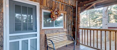 A wooden porch with a bench and a door with a window.