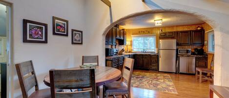 Una cocina con armarios de madera, una mesa de comedor con sillas y un refrigerador.
