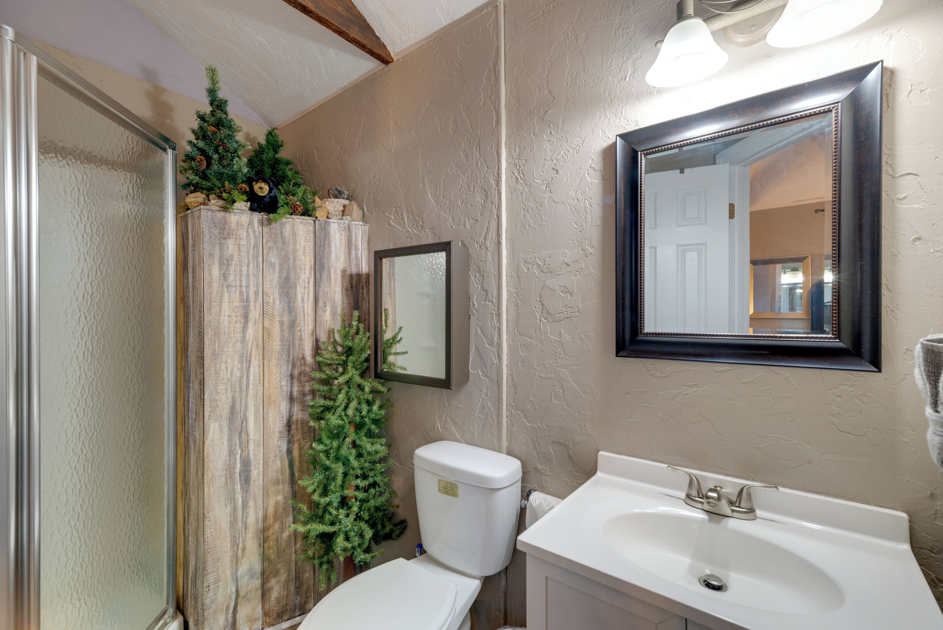 A bathroom with a toilet, sink, mirror, and a small Christmas tree decoration.
