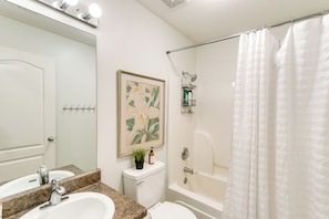 A bathroom with a sink, toilet, and bathtub. There is a shower curtain, a framed picture on the wall, and a small shelf with toiletries. - Pet-friendly Darien Vacation Rental w/ Patio! (Darien)