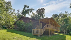 A wooden cabin with a balcony and a separate shed, surrounded by lush greenery.