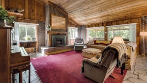 A cozy log cabin interior with a fireplace, wooden walls, and a red carpet.