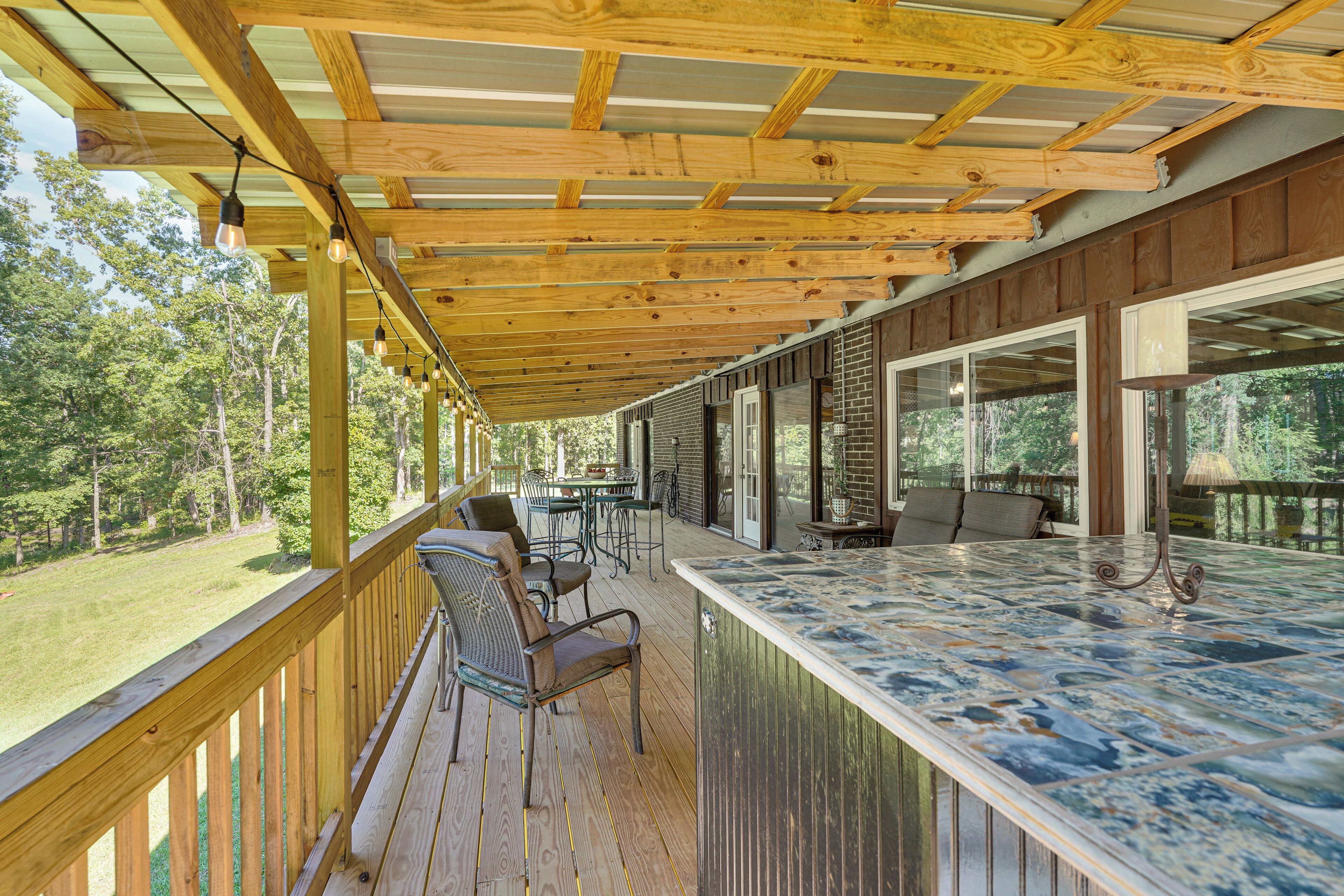Un espacio al aire libre techado con una terraza de madera, una barra con encimera de mármol y una zona de estar con sillas y una mesa.