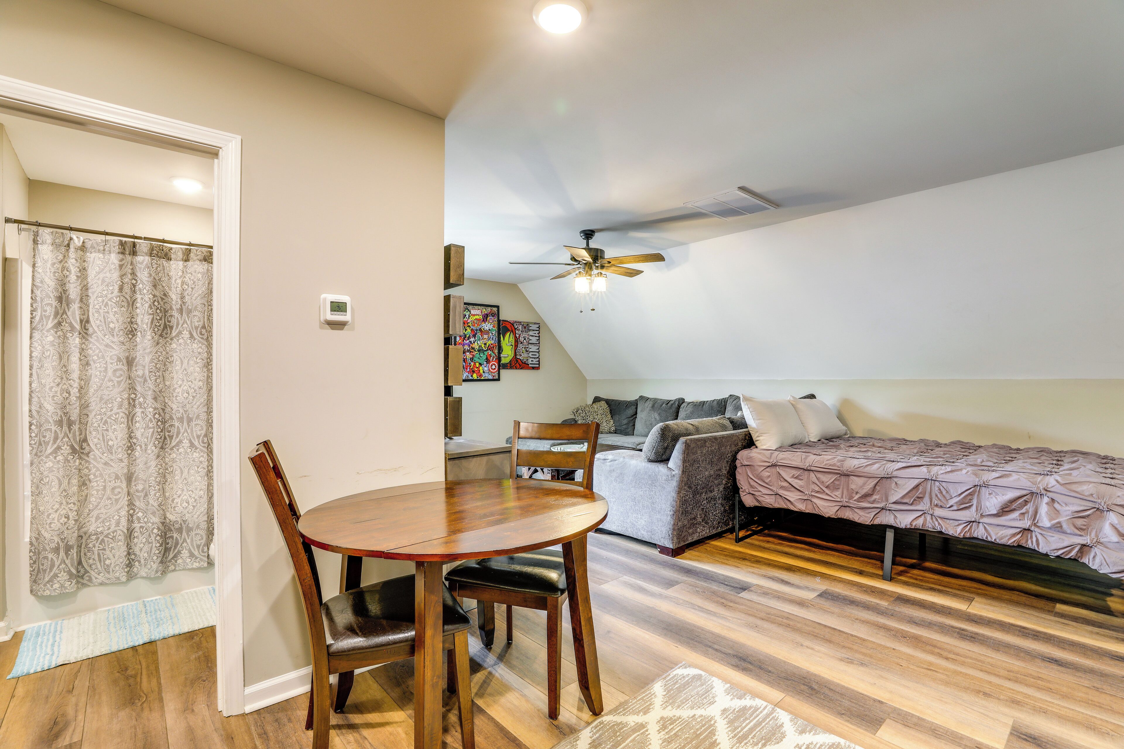 A compact room with a dining table, a sofa, a bed, and a ceiling fan.
