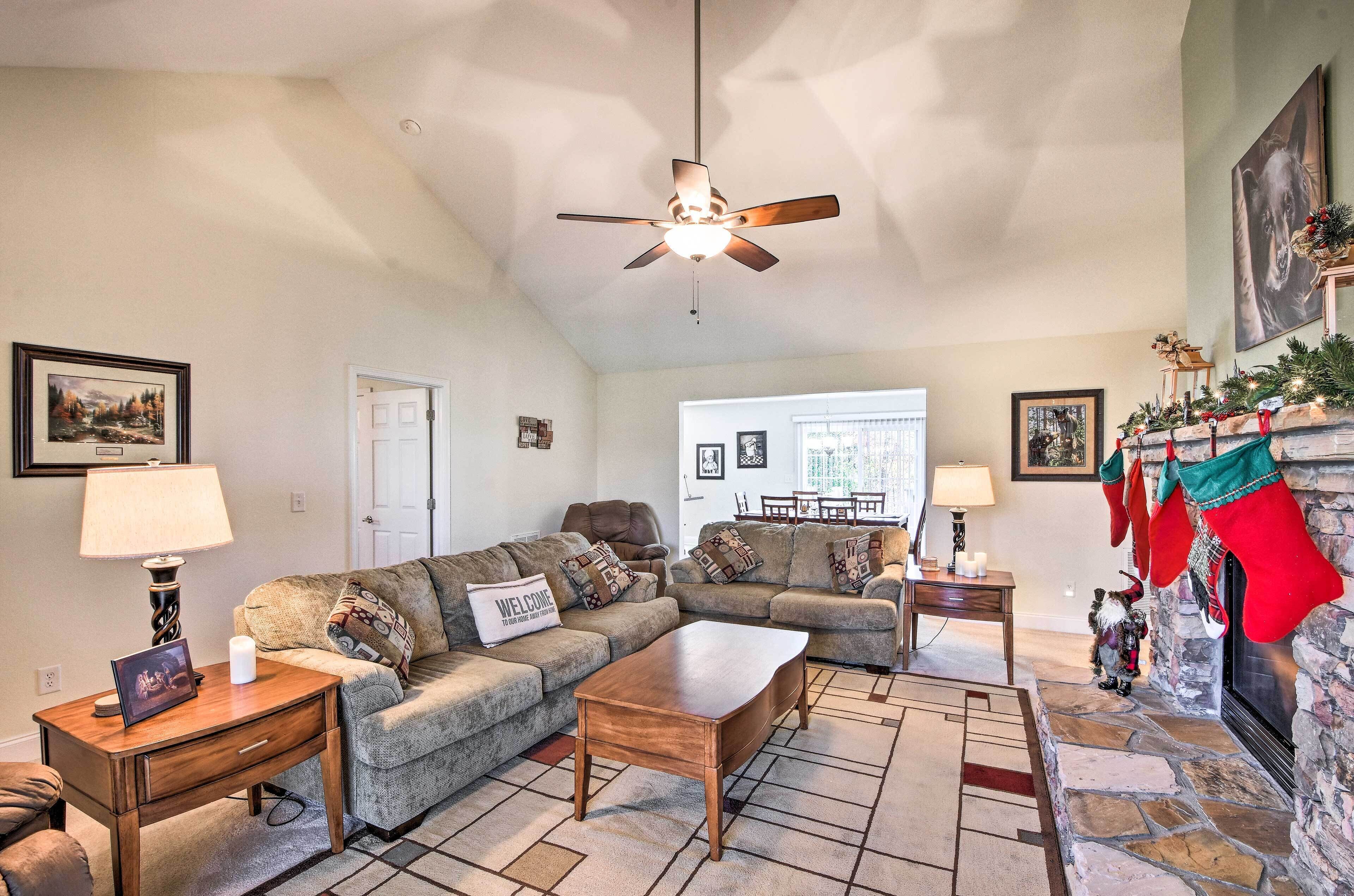 A cozy living room with a sectional sofa, a coffee table, a fireplace with stockings, and a ceiling fan.