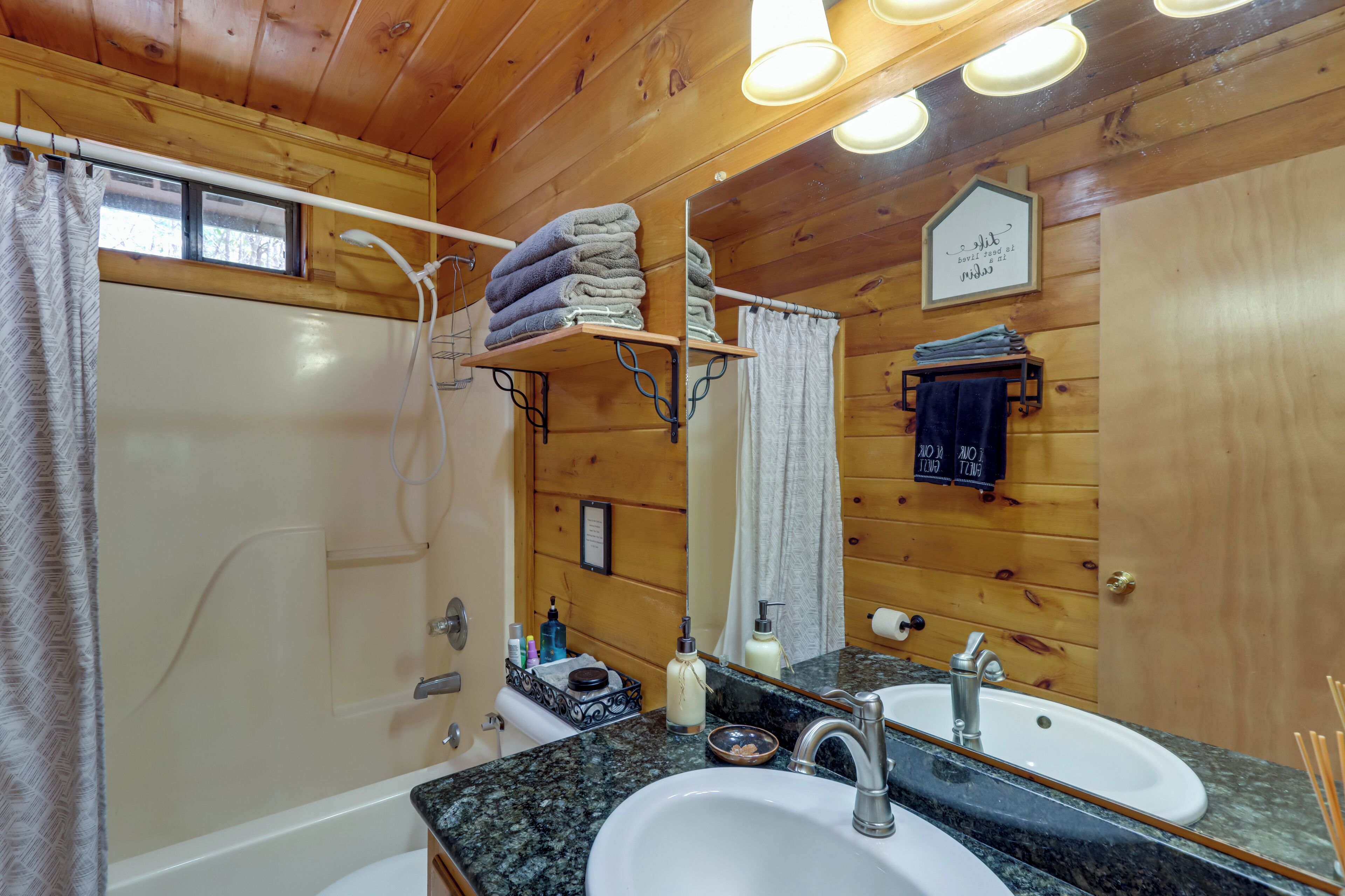 A wooden cabin bathroom with a shower, two sinks, a mirror, and a towel rack.