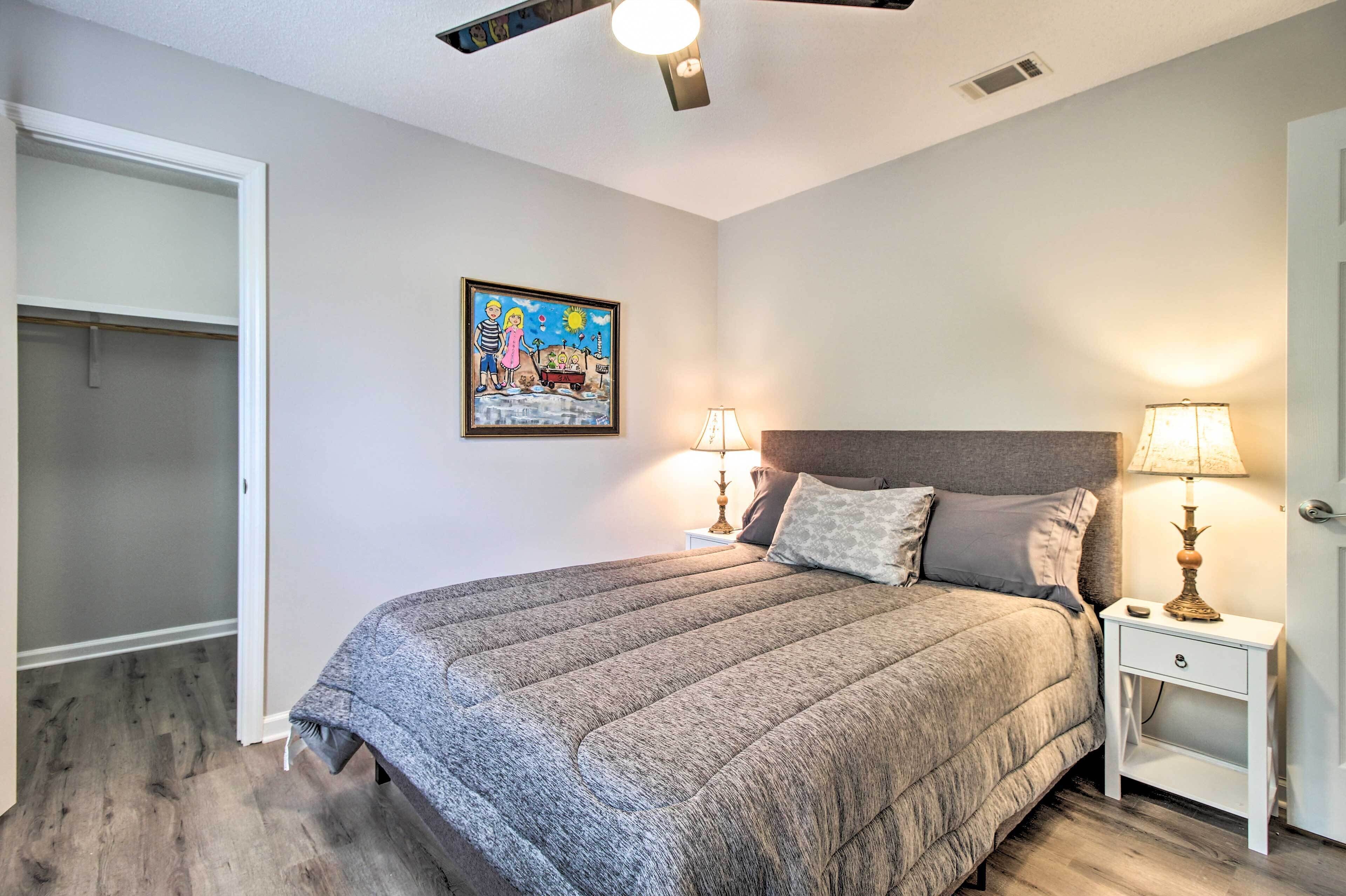 Une chambre à coucher avec un lit, des tables de chevet, un ventilateur de plafond, un tableau et un placard.