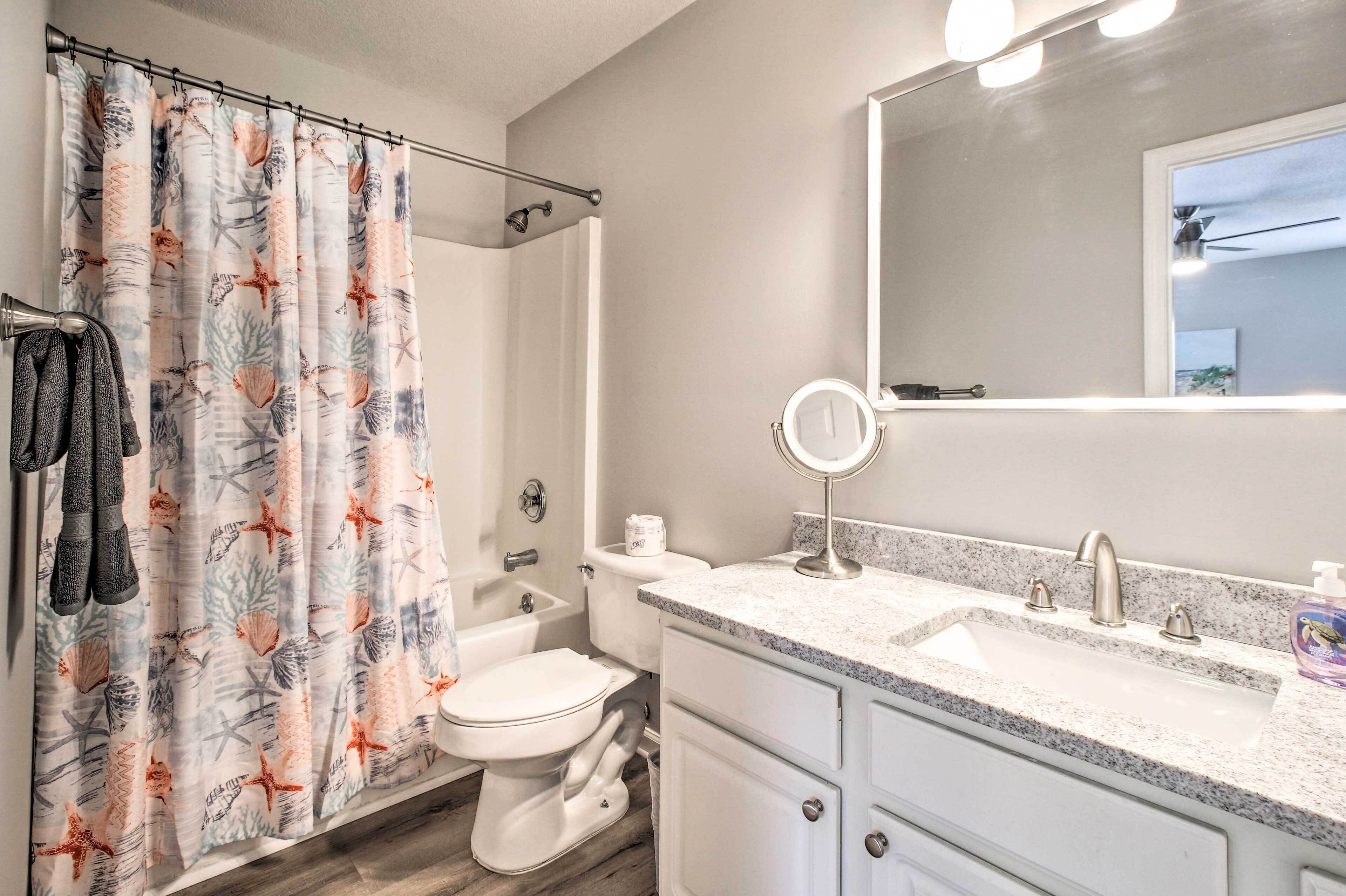 A bathroom with a shower curtain, toilet, sink, and mirror.