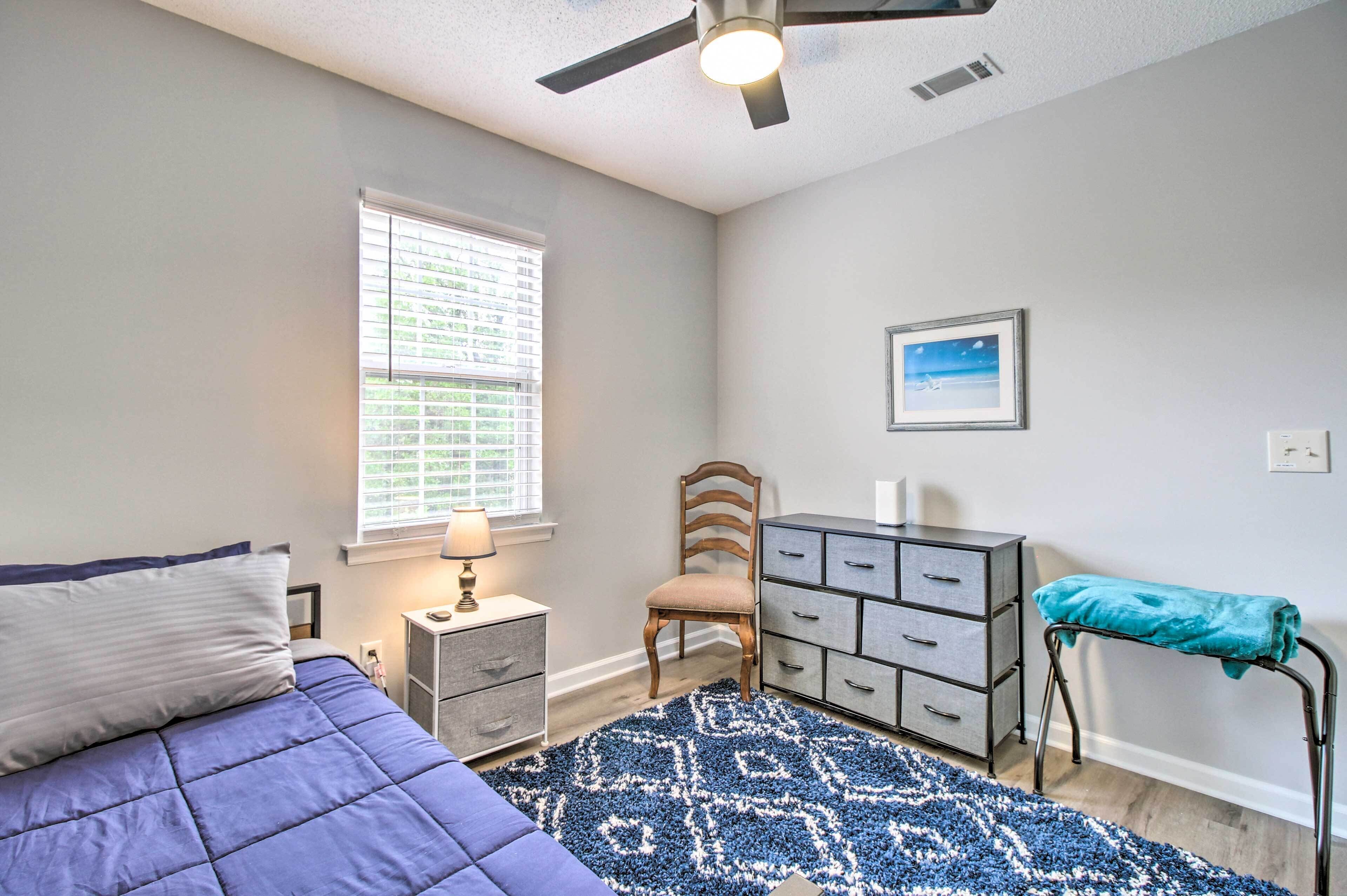 A bedroom with a bed, dresser, chair, and a window with blinds.