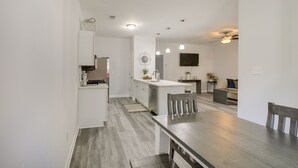 Une cuisine moderne avec des meubles blancs, un coin repas avec une table et des chaises en bois, et un espace de vie avec un canapé et un téléviseur.