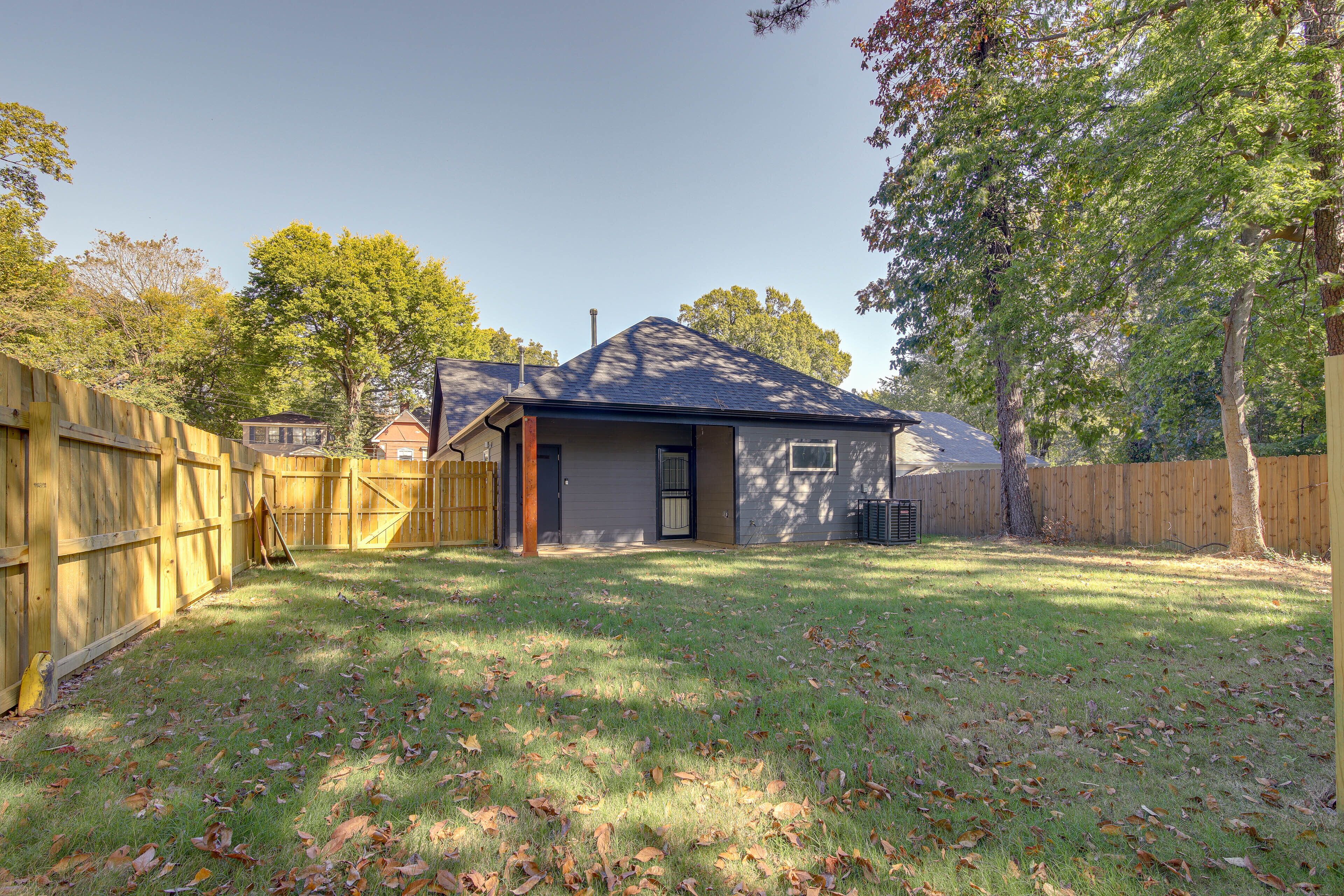 A backyard with a wooden fence, a small shed, and a grassy area with fallen leaves.