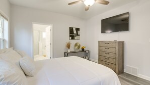 Une chambre à coucher avec un lit, un ventilateur de plafond, une télévision, une commode et un miroir.