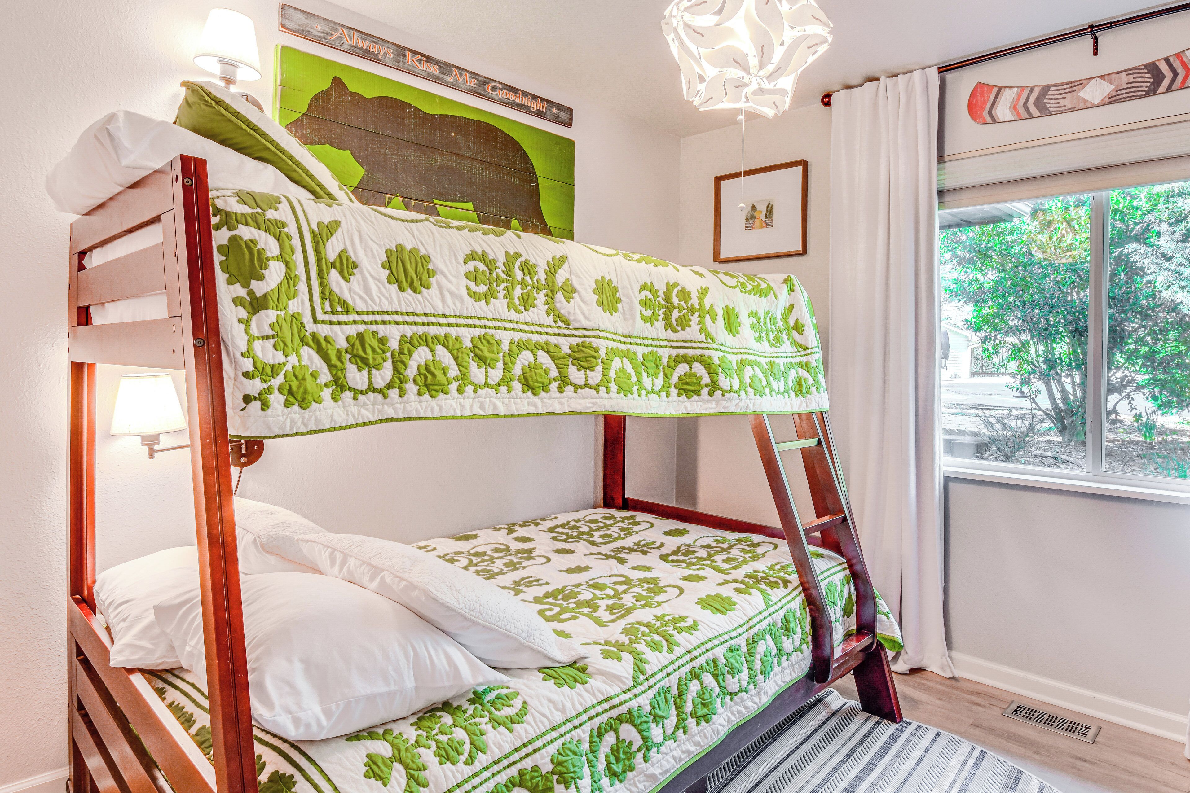 A bunk bed with a green and white patterned bedspread, a wooden headboard, and a window with a view of trees.
