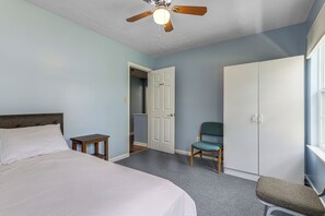 Ein Schlafzimmer mit einem Bett, einem Sessel, einem Kleiderschrank und einem Deckenventilator.