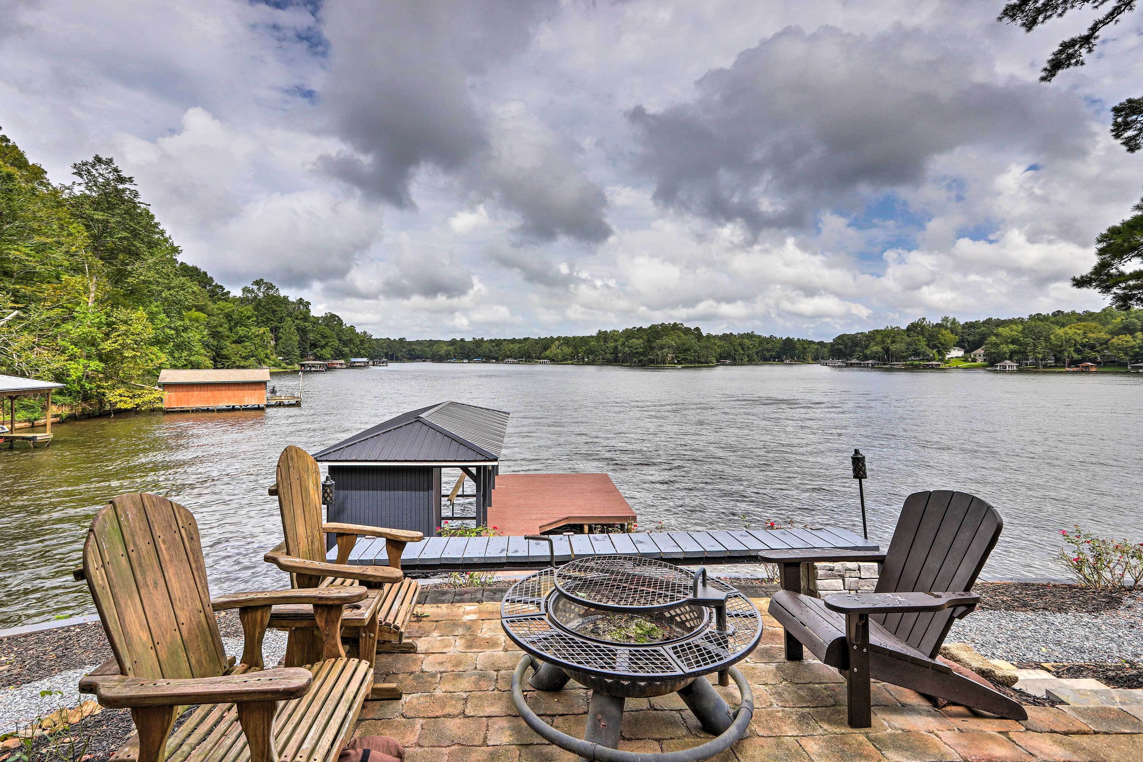 Een terras aan het meer met Adirondack-stoelen, een vuurkuil en een kleine tafel.