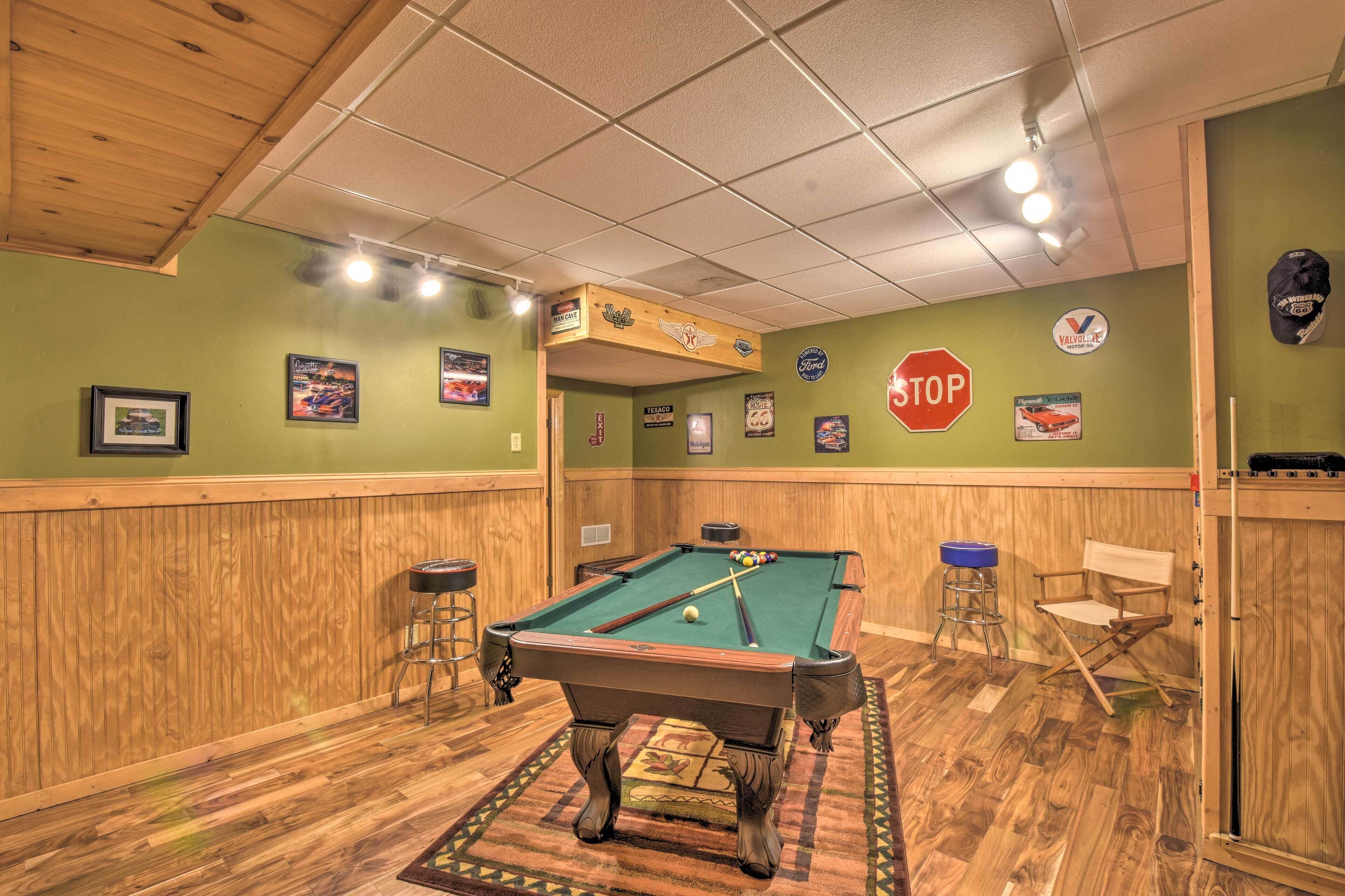 A pool table in a room with wooden paneling, a bar stool, a director's chair, and various framed pictures on the walls.