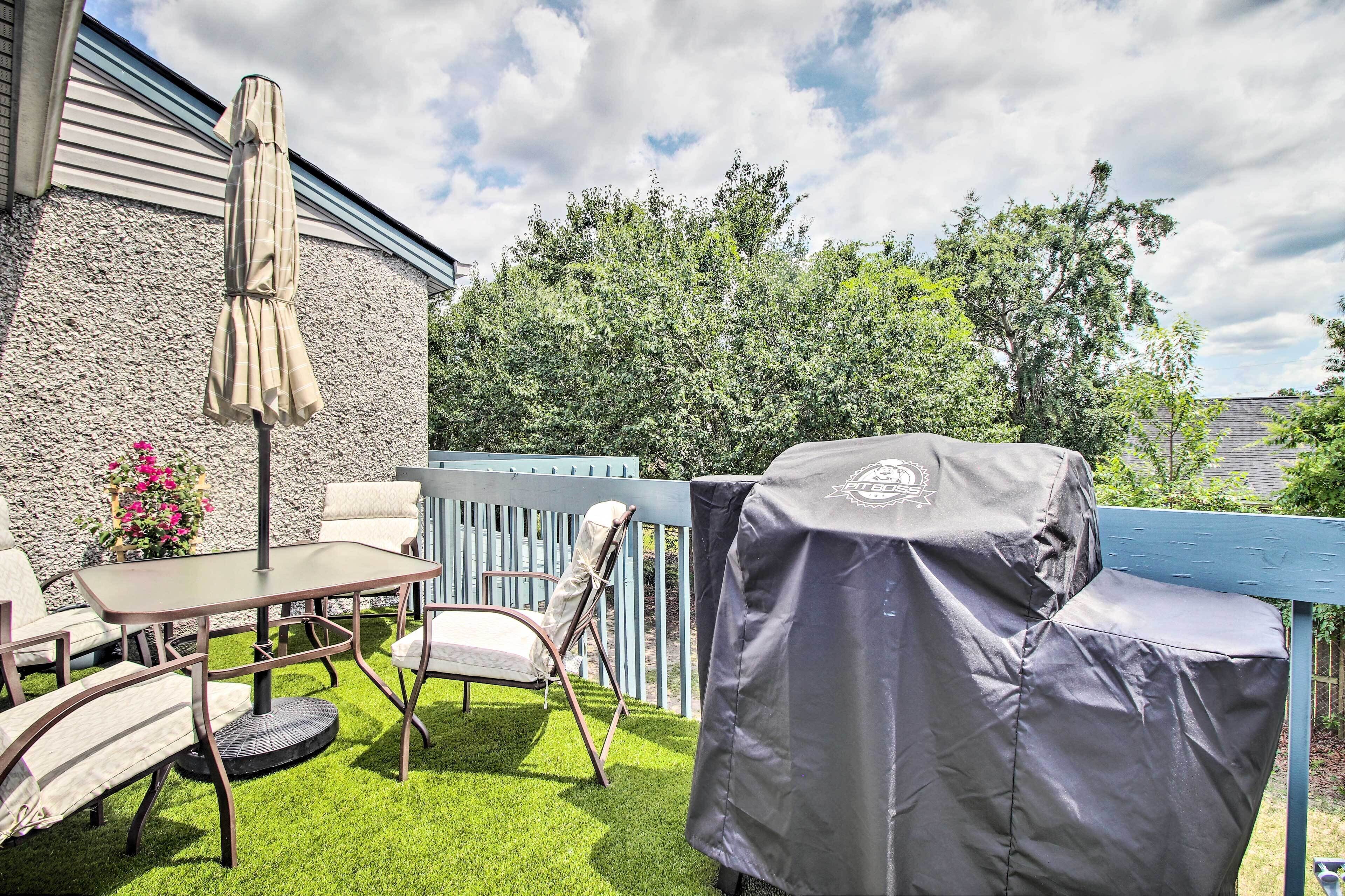 Een terras buiten met een tafel en stoelen, een overdekte barbecue en een parasol.