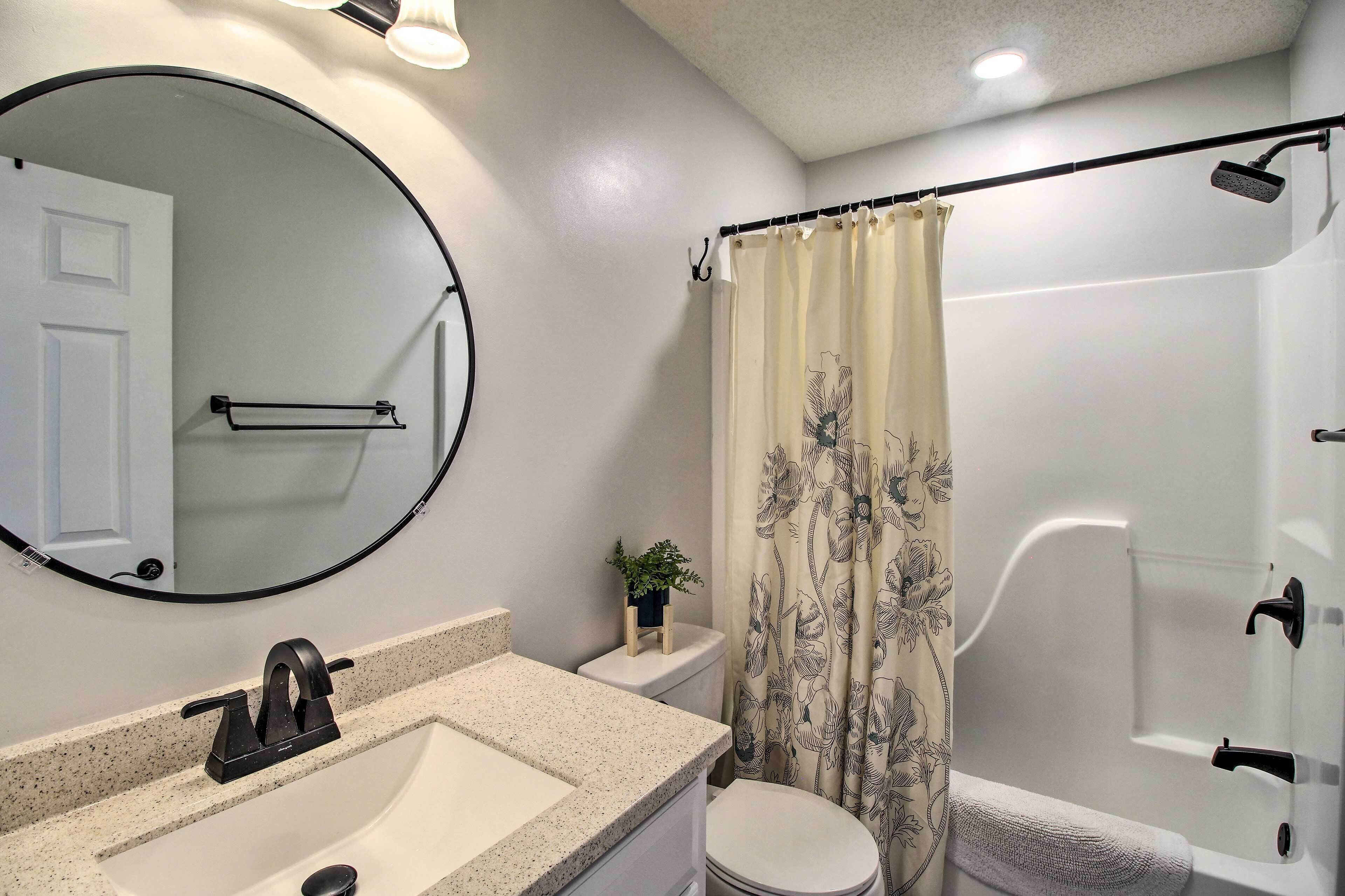A bathroom with a round mirror, a sink, a toilet, a shower, and a curtain with floral patterns.